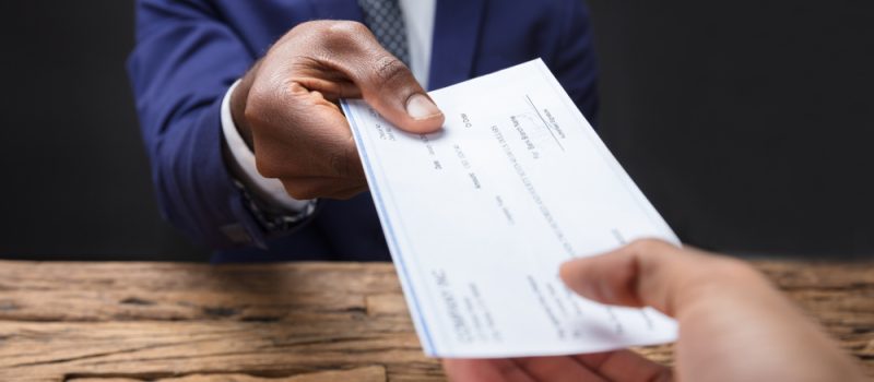 Close-up,Of,A,Businessman's,Hand,Giving,Cheque,To,Colleague,Over